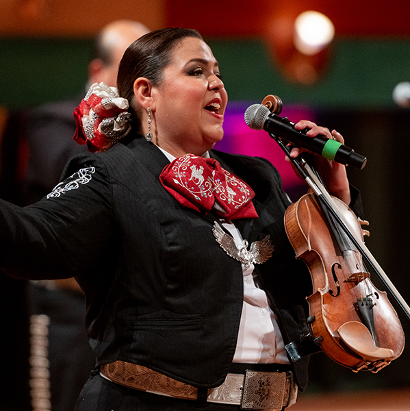 Woman sings with her violin onstage with her mariachi band