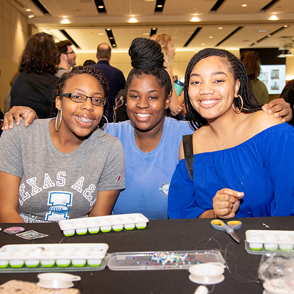 Three female students smile for the camera at a womens history month event in one of the UC Ballrooms