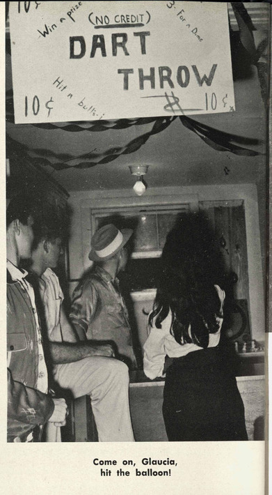 A young woman throws a dart at a school function. The hand written sign shows it is 10 cents and says '(NO CREDIT)'