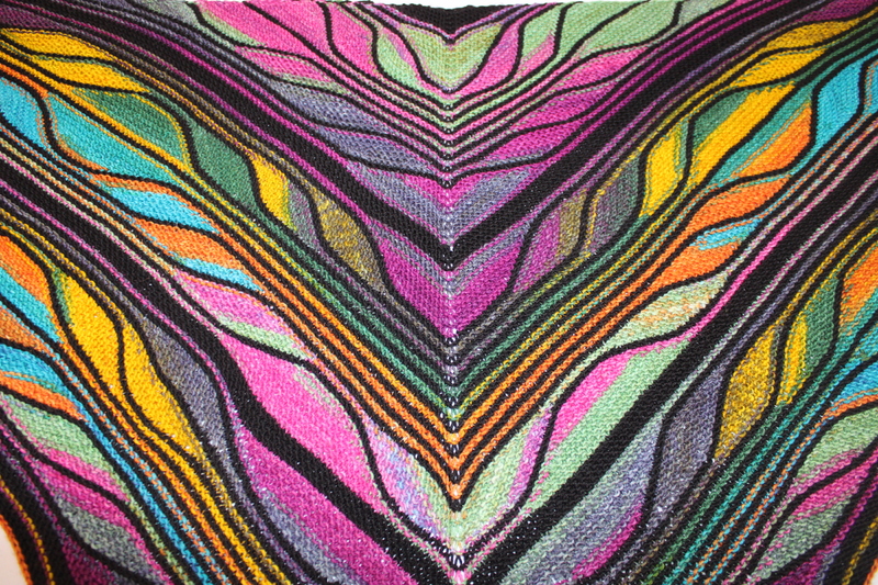 A colorful knitted fabric with V-shaped stripes in black, pink, purple, yellow, green, blue, and orange draped on a white surface.