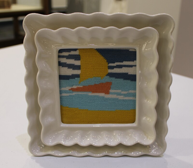 Ornate ceramic frame with needlepoint of a sailboat on water.
