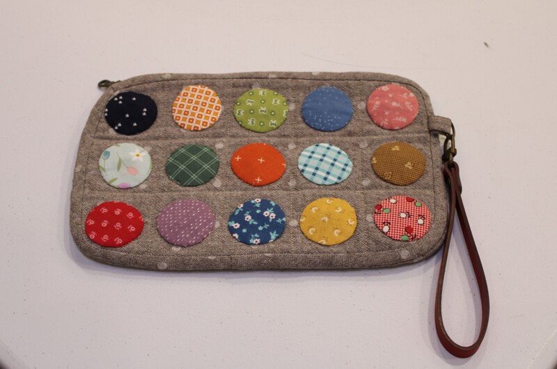 Quilted pouch with colorful circular patterns and a brown wrist strap.