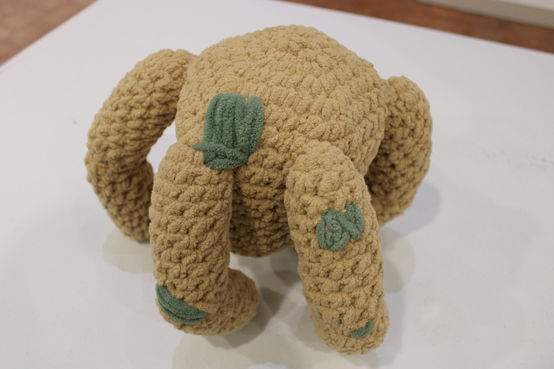 The image shows a plush, crocheted piece resembling an abstract creature with multiple legs. The shape appears organic, with a central bulbous body and several curved appendages extending outward, similar to tentacles. The character is Rocky the Eridian from Andrew Weir's Project Hail Mary