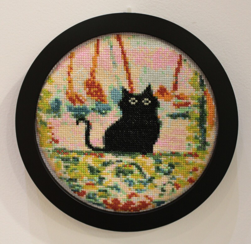 Embroidery hoop with black cat cross-stitch art in pink floral background.