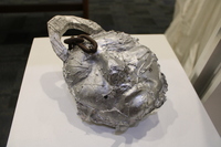 Metallic sculpture resembling an abstract face with rusty chain embedded.
