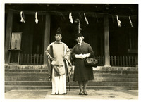 A man in traditional Japanese clothing and a woman in Western attire stand on steps outside a building. 