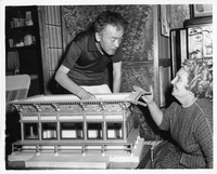 Two people examine an architectural model of a traditional Asian building.