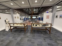 Art exhibition space with various artworks on walls, pedestals, and tables.