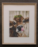 Framed cross stitched piece portraying a cow with it's tongue out. There is greenery on the cow's head.