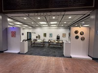 Art exhibition space with various artworks on walls, pedestals, and tables.