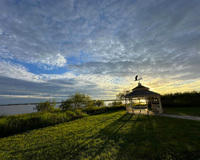 Gazebo on a grassy lawn near a lake at sunset with a cloudy sky.