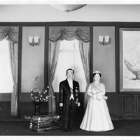 Dolls in formal attire in an elegant room with draped windows and a painting of a snowy landscape.