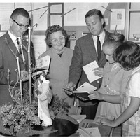 Group of adults and children examining a display with a model tree and a figurine.