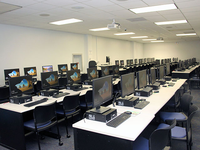 Computer Lab 2 showing rows of computers, tables, and chairs. Including projector and large white walls
