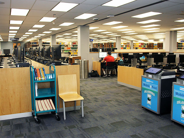 Computers, tables, chairs, and printers located near the Ask Us Desk on the first floor of the library