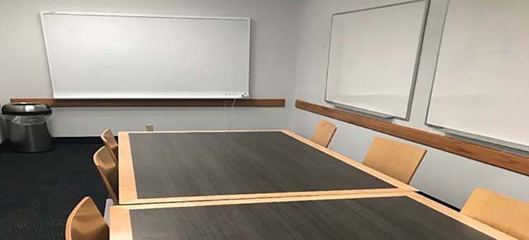 Large study room with two white boards, two tables, one smart board, and eight chairs