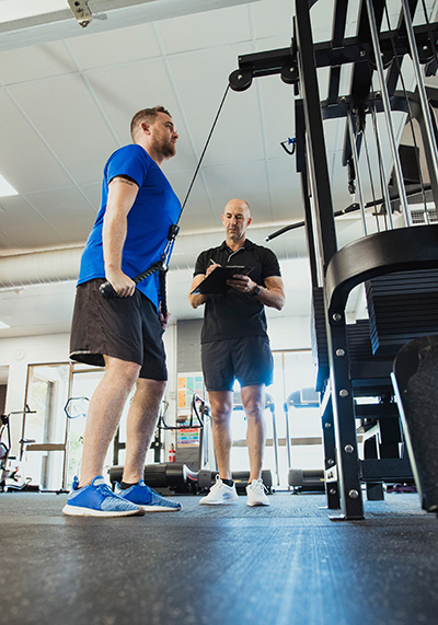 Man using training equipment to lift weights with trainer taking notes.