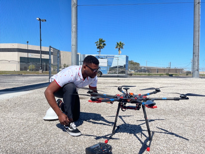 A photo of a male student kneeling in front of drone entitled 'Innovation at its best'