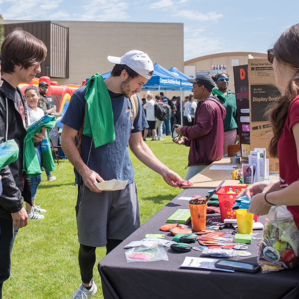 A male student outside at an event looking at a table that has small giveaway items